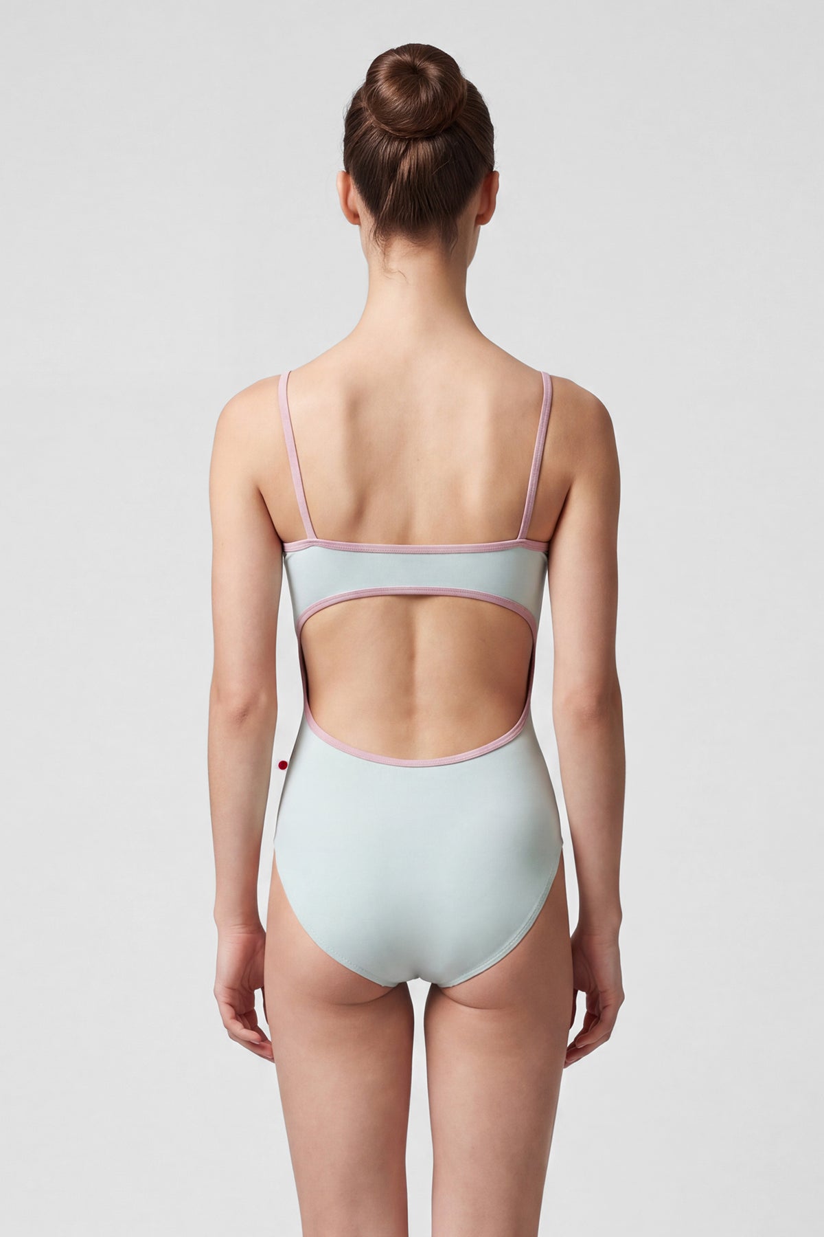 AI-generated model. Kiki leotard, pale sage-green with a ruched V-neck and dusty-pink strap trim.