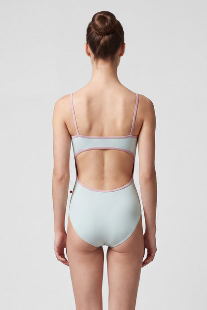 AI-generated model. Kiki leotard, pale sage-green with a ruched V-neck and dusty-pink strap trim.
