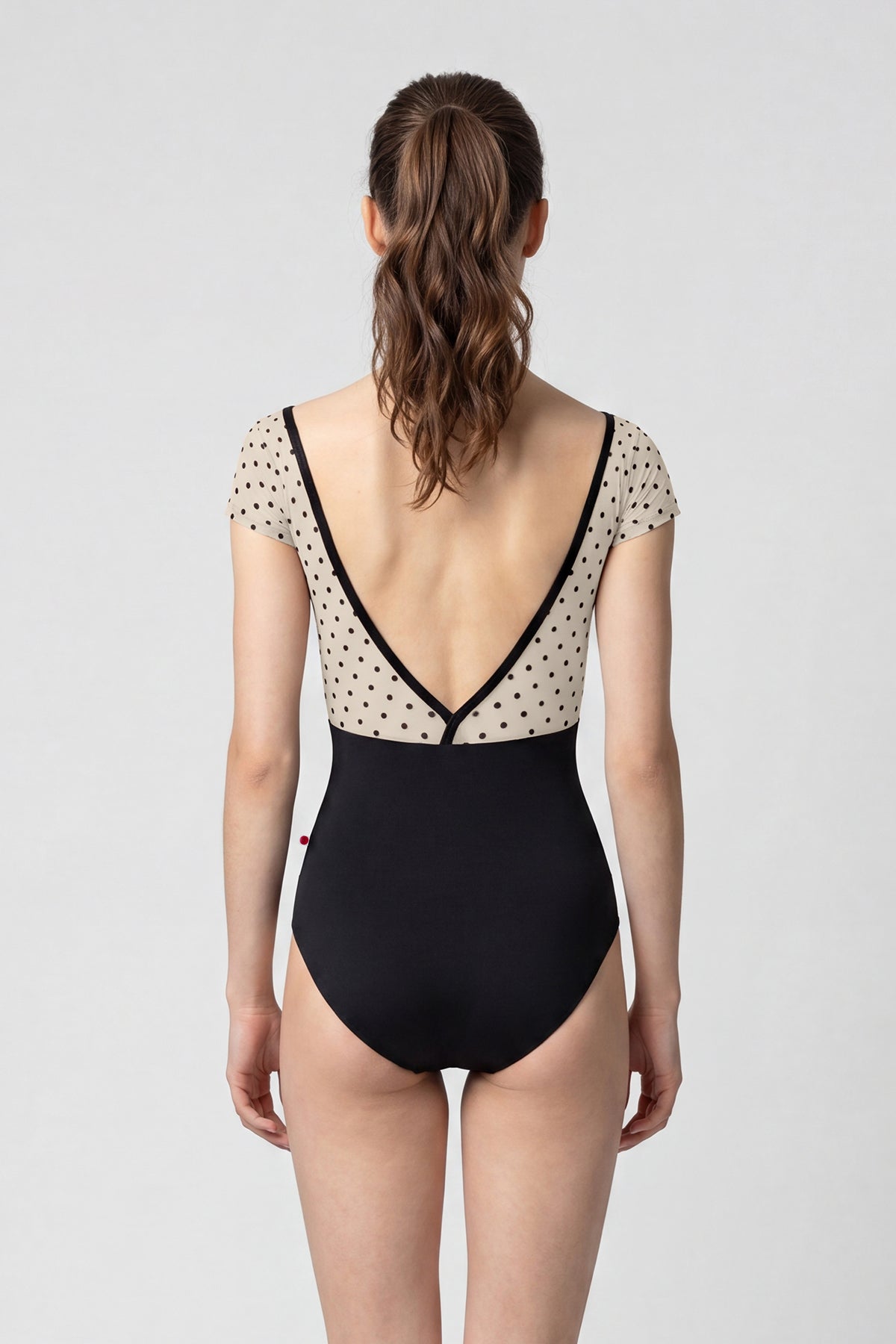 AI-generated model. Alicia leotard, cream polka-dot cap-sleeve bodice with black V-neck trim and black body.
