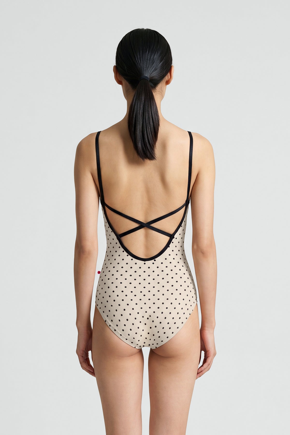 AI-generated model. Daniela leotard, all-over cream polka-dot with thin black straps and black neckline trim.
